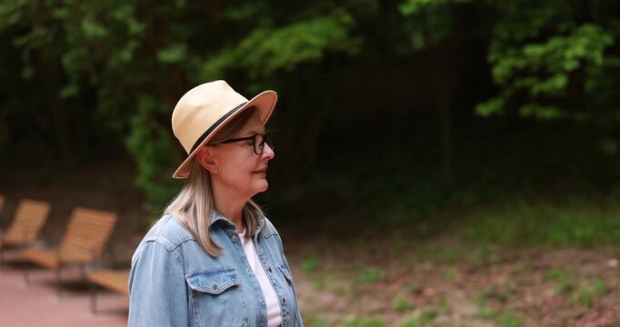 Beautiful senior woman with straw hat walking in spring park
