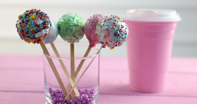 Tasty cake pop and cup of drink on pink wooden table, closeup. Camera moving forward