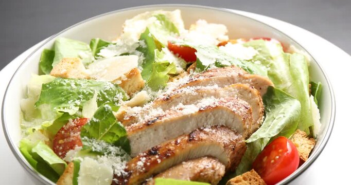 Tasty Caesar salad with chicken on black table, rotating