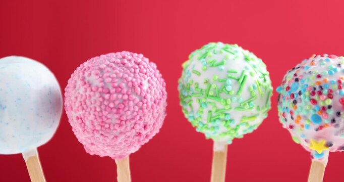 Tasty cake pops on red background, closeup. Camera moving right