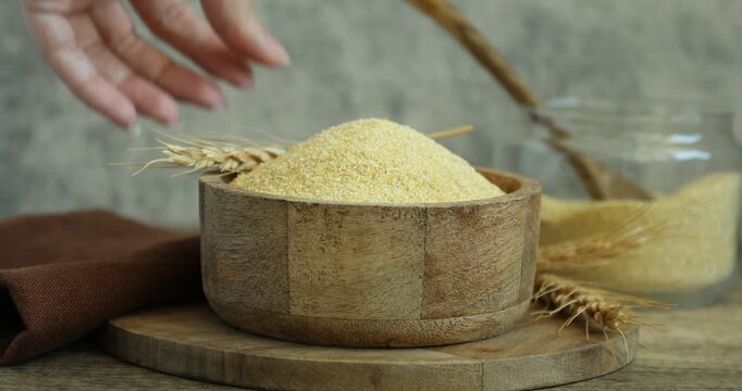 Woman putting spike onto bowl with semolina at wooden table, closeup