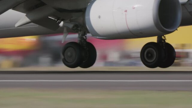 Close up of aircraft main landing gear and turbofan engine rolling on runway at high speed, narrow body jet, blurred background with blue fuselage detail, runway surface visible