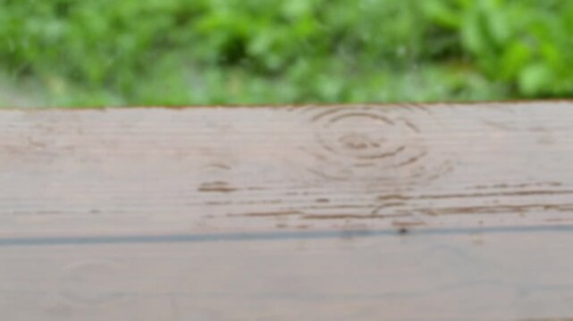 Rain falling on wooden stairs, starting out fully blurred and transitioning out from the blur to show the splashes, in slow motion