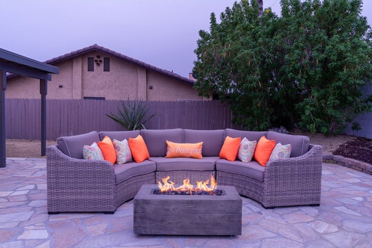 Outdoor wicker patio set sectional, pillows and fire table at dusk