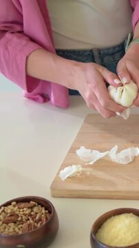 Vertical video: Peeling cook in pink holding garlic over board at home preparing to chop with knife