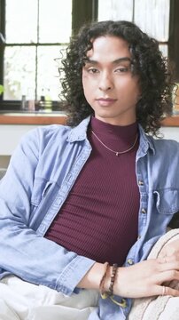 Vertical video: Responding camera nonbinary in maroon top shifting on sofa adjusting bracelets