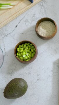 Vertical video: Panning top-down camera revealing bowl of edamame on marble counter to show food