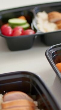 Vertical video: On play, camera panning across black meal trays with grain, sliced protein for prep