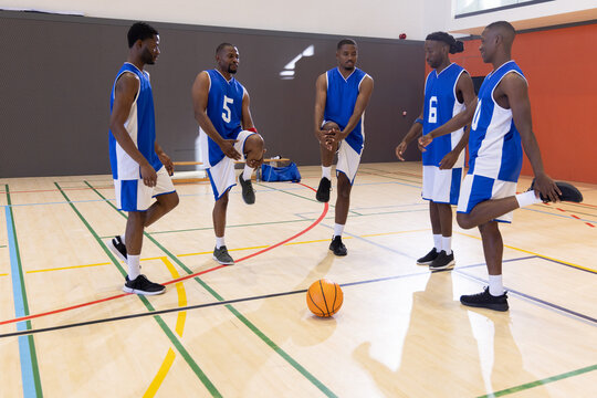 African American male team stretching at center court around orange ball in blue jerseys