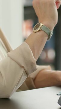 Vertical video: Arm lifting white pen to lips during office chat, checking green watch, copy space