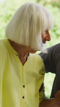 Vertical video: Leaning senior in pale yellow blouse responding to partner touch by glass door