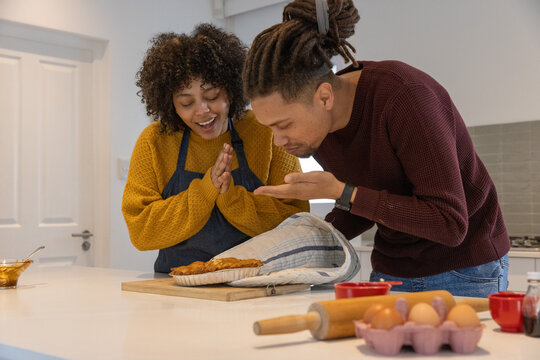 African American couple smelling pie at kitchen island wearing knit sweaters and holding oven cloth