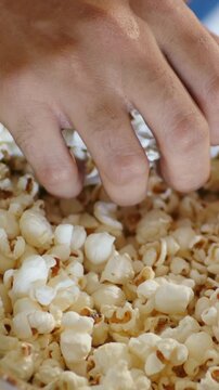 Vertical video: Reaching hand scooping popcorn in large bowl on wooden table, taking snack