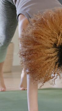 Vertical video: Camera pulling back, woman in gray top stretching into fold on green mat with watch