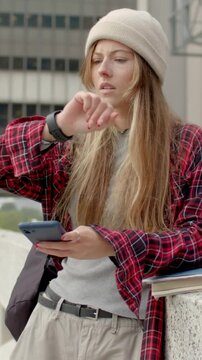 Vertical video: Tapping plaid lady checking watch placing phone notes in bag at rail walking right