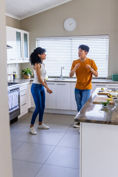 Diverse couple noticing halved avocado on cutting board, preparing breakfast in home kitchen