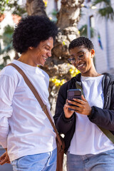 African American couple leaning together and smiling while showing smartphone in front of palm tree © wavebreak3