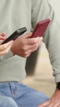 Vertical video: Holding still then tapping phones, two adults in jeans on bench comparing screens