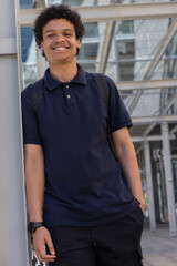 Adult African American man leaning on metal column at plaza wearing navy polo backpack, copy space © wavebreak3