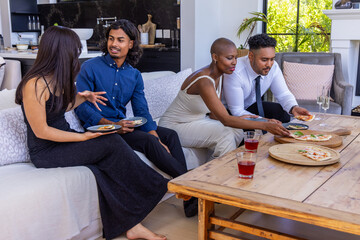 Obraz premium Diverse friends sitting on light sofa in living room, in smart outfits sharing wooden pizza boards