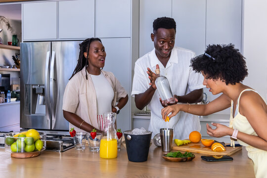 African American friends preparing cocktails at kitchen island, using clear bottle and metal shaker