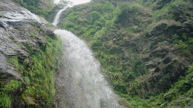 Waterfall flowing down a steep rocky cliff covered with greenery in mountains