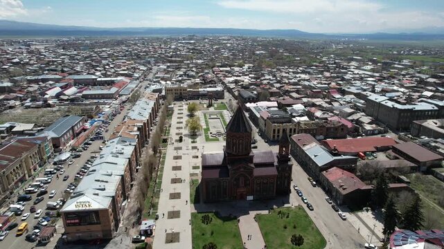 An aerial drone shot of the historic Holy Saviour Church in Gyumri, Armenia, showcasing its unique black tufa stone architecture and the surrounding cityscape on a sunny day.


