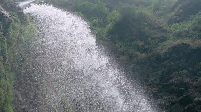 Waterfall flowing down a rocky cliff in misty mountain environment