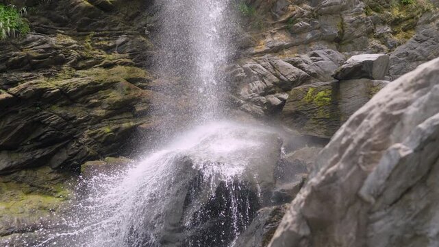 Cinematic panning shot of a beautiful waterfall flowing over rocks in a lush forest