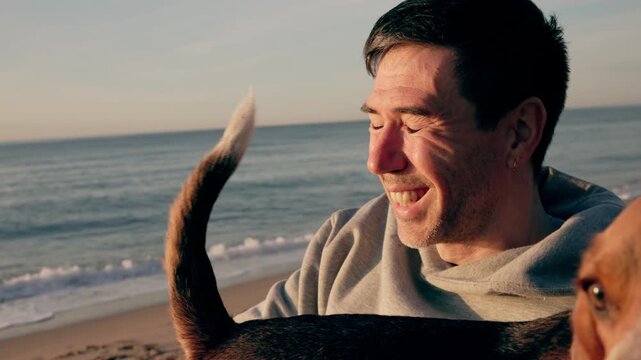 adult man enjoying a beautiful sunset on the beach, laughing and playing with his beloved dog while its tail wags with joy, creating a heartwarming scene of companionship and freedom