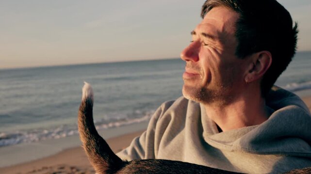 adult man enjoying a beautiful sunset on the beach, laughing and playing with his beloved dog while its tail wags with joy, creating a heartwarming scene of companionship and freedom
