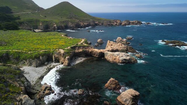 Aerial drone footage of the dramatic coastline at Point Lobos in Big Sur, California. The shot captures rugged cliffs, turquoise Pacific Ocean waves, rocky coves, and untouched natural landscapes.