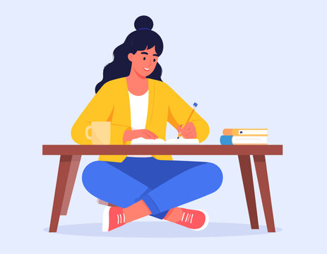 Young woman sitting on floor writing at a low table with books and a mug, engaged in study or work.