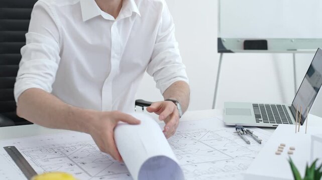 Architect drawing building plans on blueprints using a compass, creating a new construction project design, working on engineering and drafting tasks in an office