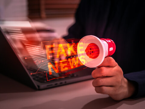 Concept of fake news and digital misinformation spreading through online media, social networks. Hand holding megaphone symbolizes cyber propaganda, AI generated content and information manipulation.