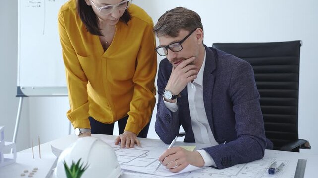 Architects and engineers reviewing blueprints and project plans at a desk, collaborating on design solutions and construction strategy in a modern professional office setting