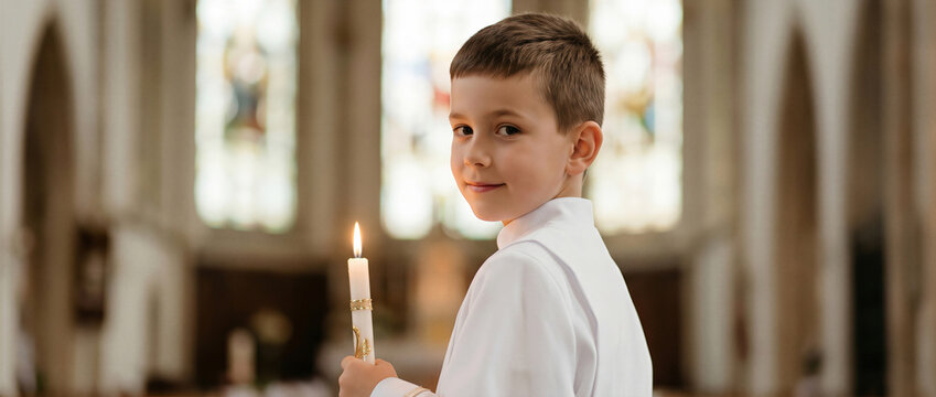 Smiling young boy in a white robe holding a lit candle inside a church