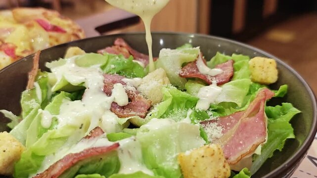 Pouring dressing on fresh Caesar salad.