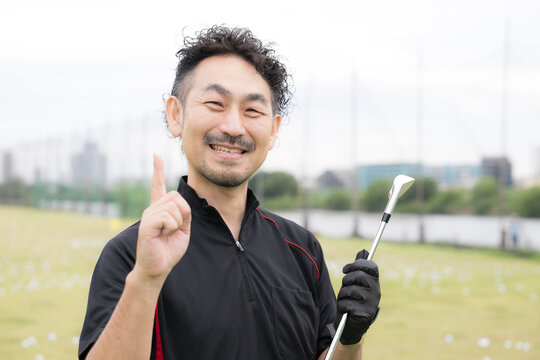 ゴルフクラブを持ちながら笑顔の男性ゴルファーのポートレートカメラ目線で指差しのポイント笑顔　ゴルフの練習