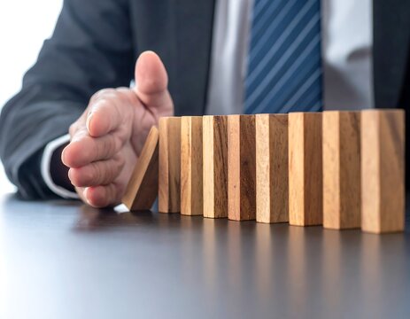 Businessman Hand Stopping Falling Wooden Domino Blocks on Office Desk