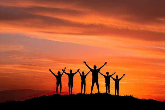Silhouettes of a joyful group of youths with arms raised celebrating a vibrant sunset atop a hill