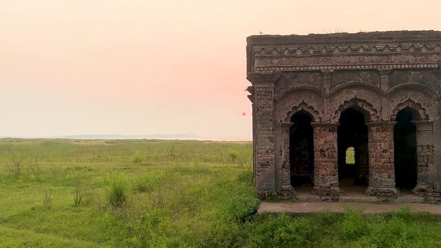 Mukutmanipur Dam In Bankura District West Bengal Ancient dilapidated hindu brick temple ruins standing in open grassy landscape near riverbank during sunset.