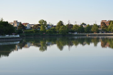 Obraz premium Peaceful Waterfront Park with Green Trees Reflected on Still Water