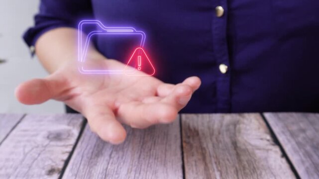 Documents at risk. Close-up of a woman's hand at a table holding a virtual folder icon and a warning sign.