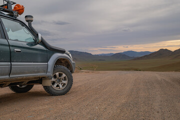 Side view of offroad SUV car parked on dirt road at sunset. Expedition 4x4 vehicle traveling through remote scenic desert valley landscape under dramatic evening sky. © ANDREY