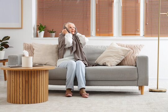 Senior woman covering her ears with plaid because of noisy neighbours at home