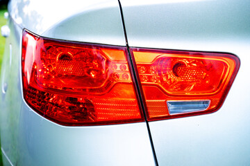 Close-up of a red tail light on a silver car, showing the rear lamp, reflective lens, vehicle body, and automotive design detail. © efiederphoto