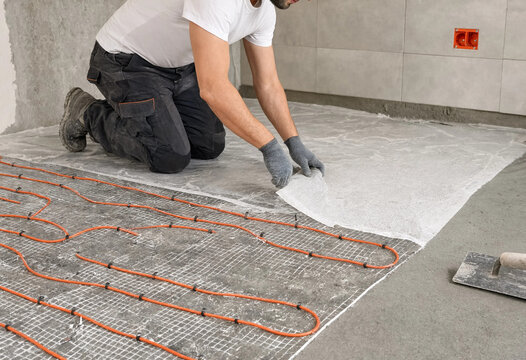 Worker installs underfloor heating system in new construction