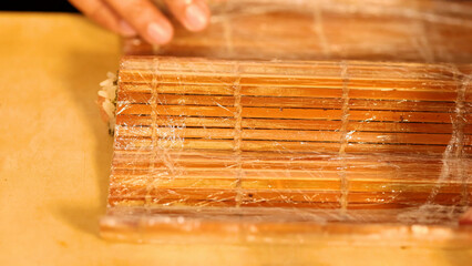 Close-up of Chef Hands Rolling Sushi with a Bamboo Mat and Plastic Wrap © blueringmedia