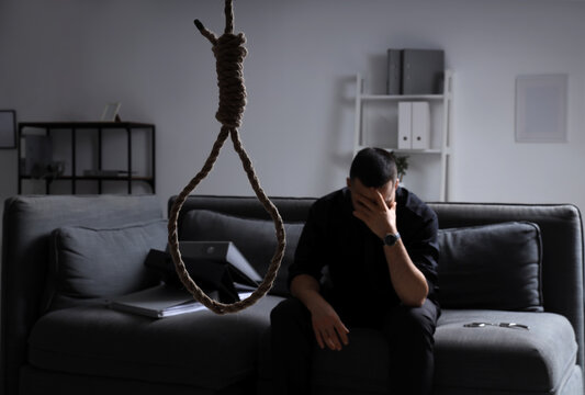 Hanging rope with loop against businessman in dark office. International Stress Awareness Week